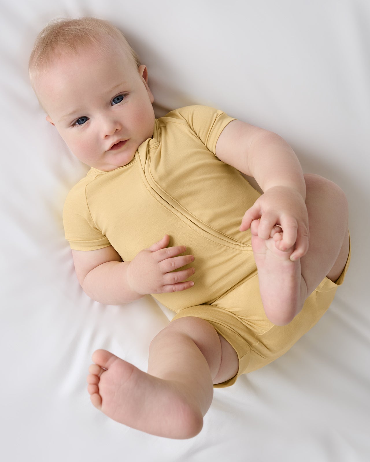 Baby lying on white bedding wearing Sunglow bamboo shorty pajamas