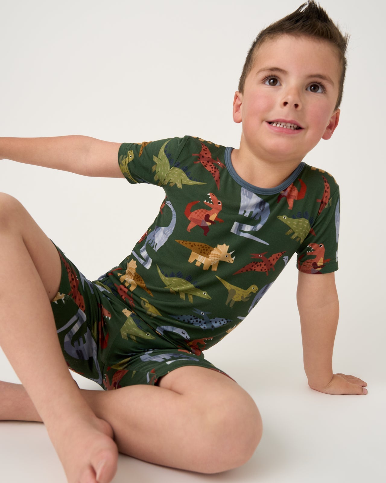 Seated boy in Dino Forest dinosaur-print bamboo pajamas