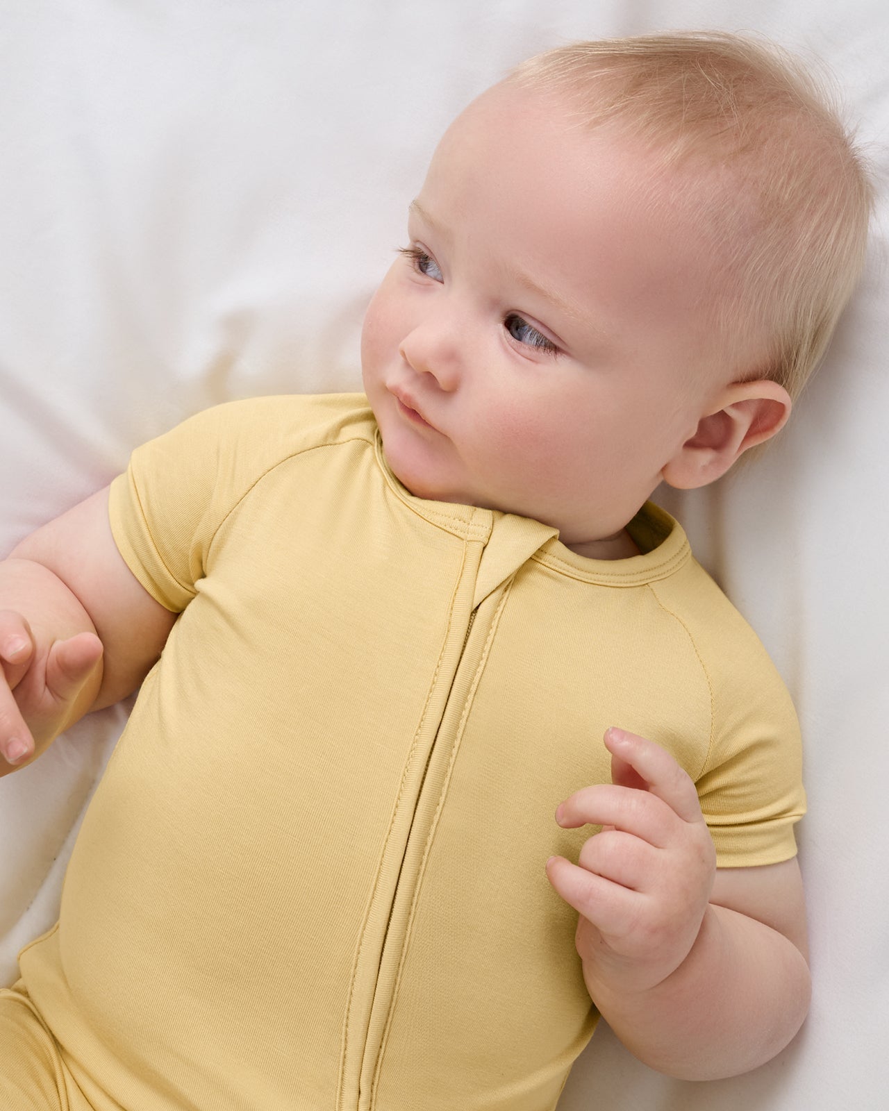 Baby resting on white bedding in Sunglow bamboo shorty pajamas